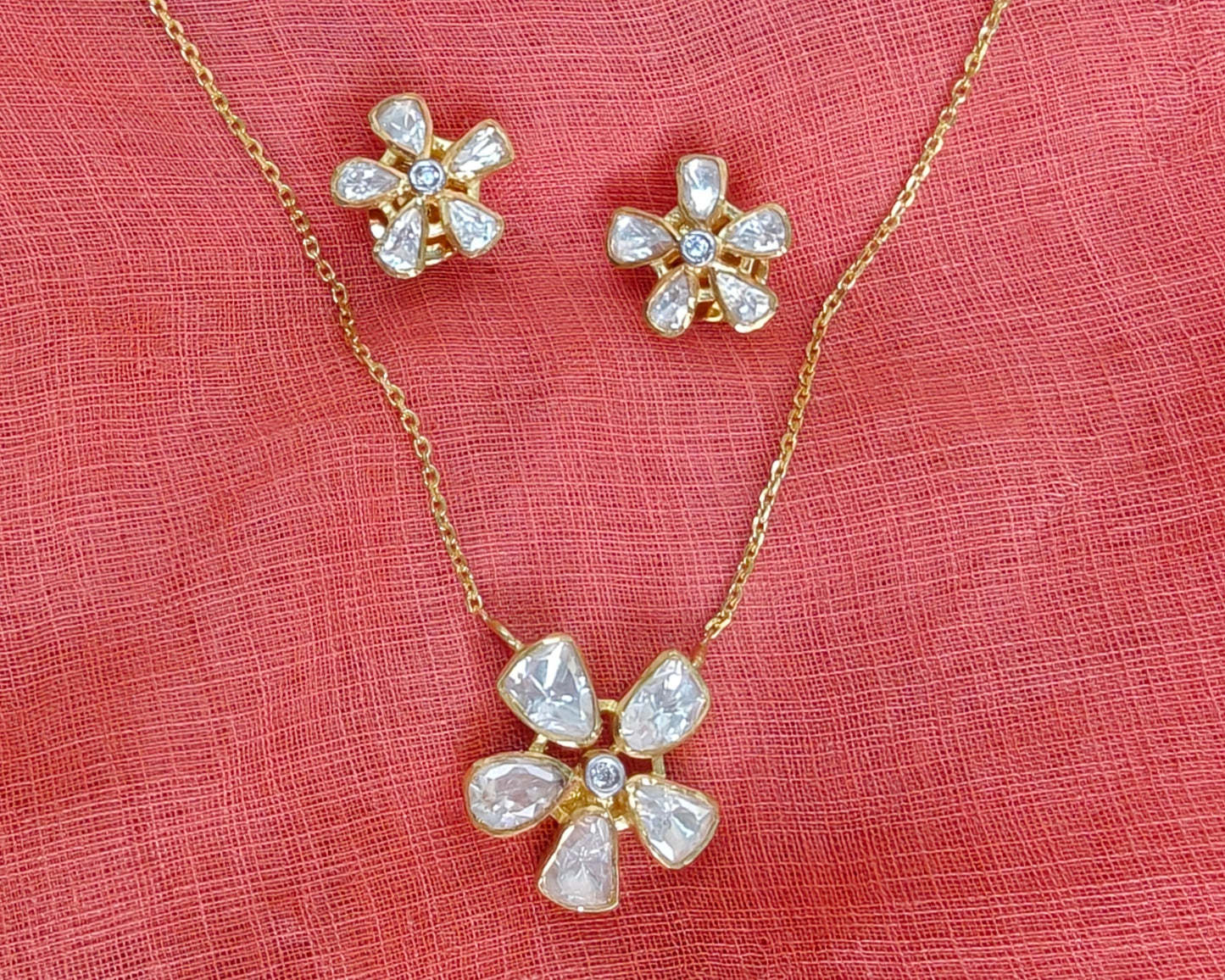 Flower-shaped jewelry set with necklace and earrings on a pink fabric background