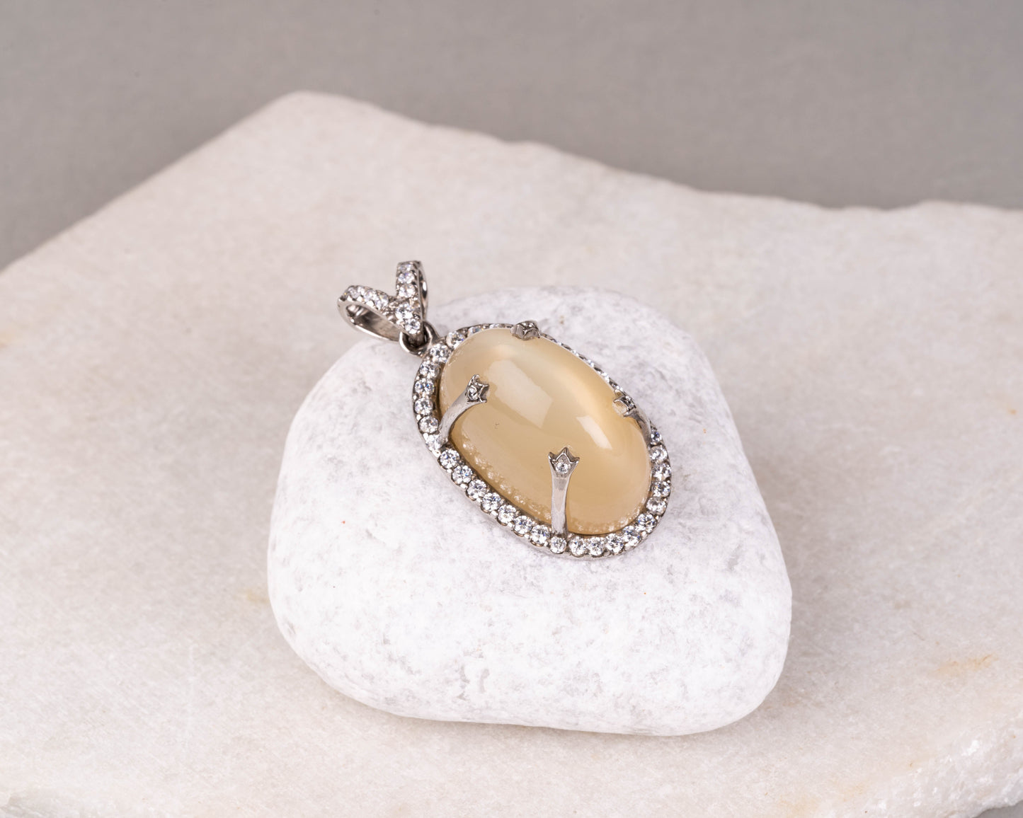 A silver pendant featuring a central moonstone surrounded by smaller clear crystals, displayed on a white polishing cloth.