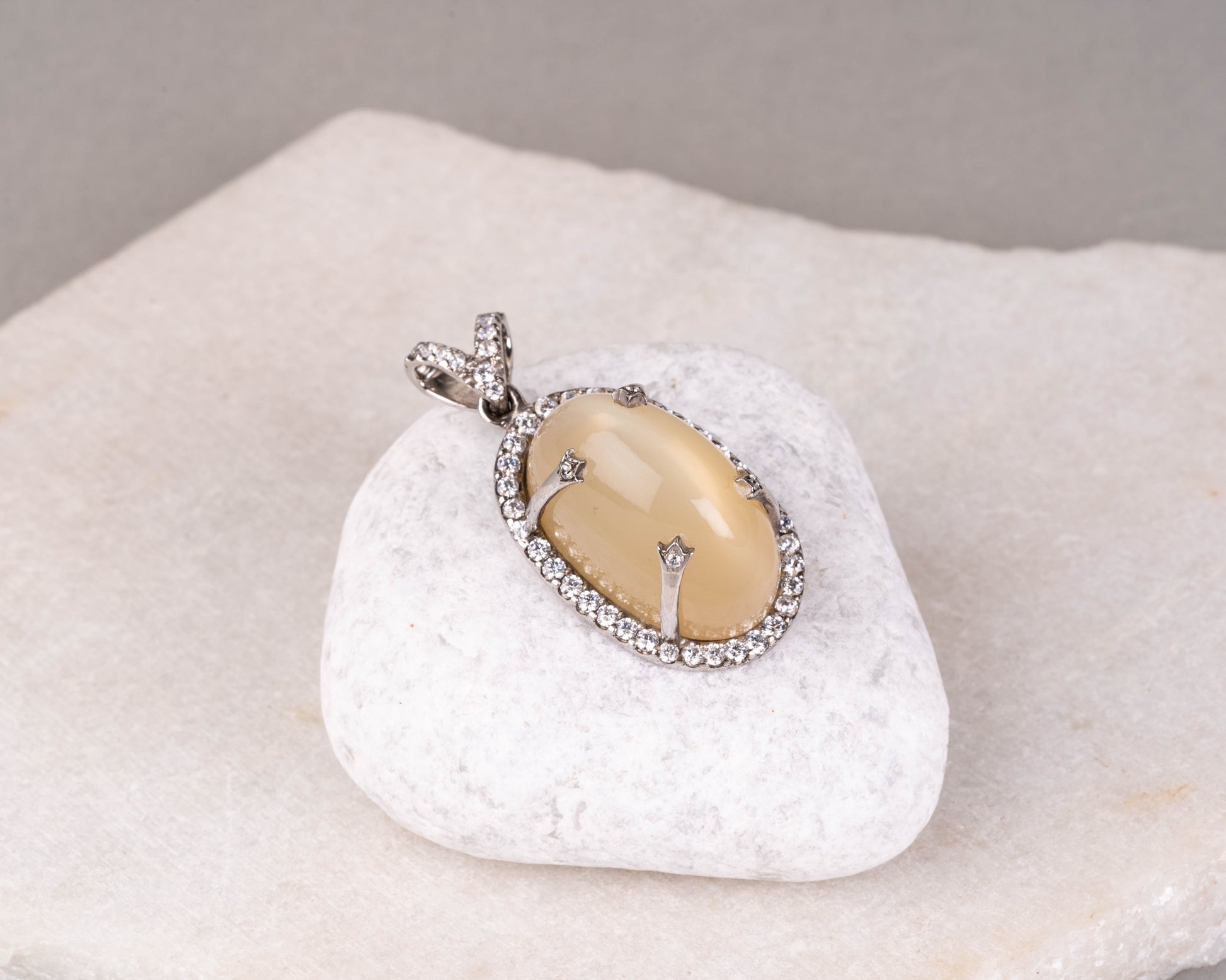 A silver pendant featuring a central moonstone surrounded by smaller clear crystals, displayed on a white polishing cloth.